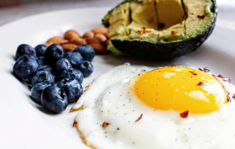 A nutritious breakfast featuring a fried egg, avocado, blueberries, and almonds.