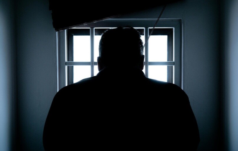 Dark silhouette of a man in a prison cell, backlit by window bars.