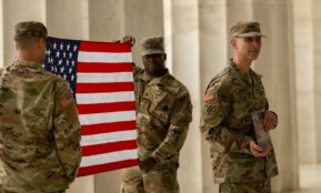 US soldiers in camouflage uniforms hold American flag at Washington DC landmark.