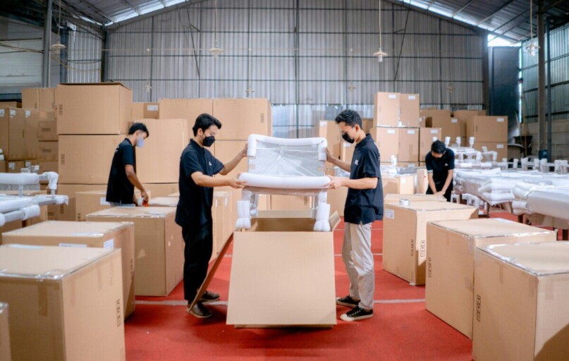 Men in a warehouse wearing masks, assembling and packing furniture into boxes with efficiency.