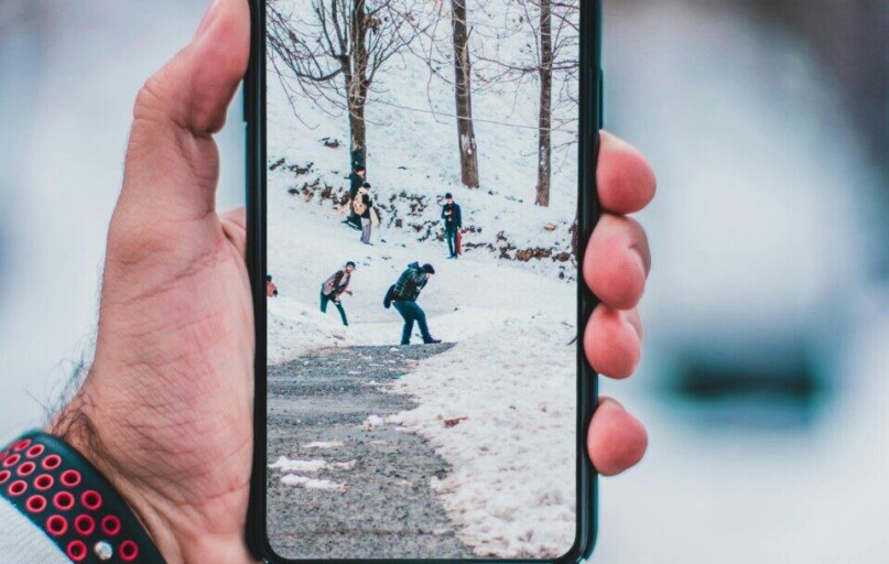 Hand holding smartphone displaying a winter scene with people walking on snow-covered path.