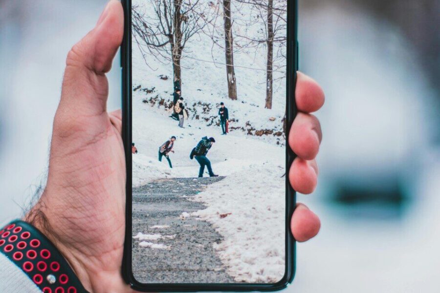 Hand holding smartphone displaying a winter scene with people walking on snow-covered path.