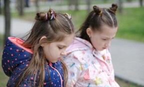 Two young girls in winter jackets, contemplative in a park setting.