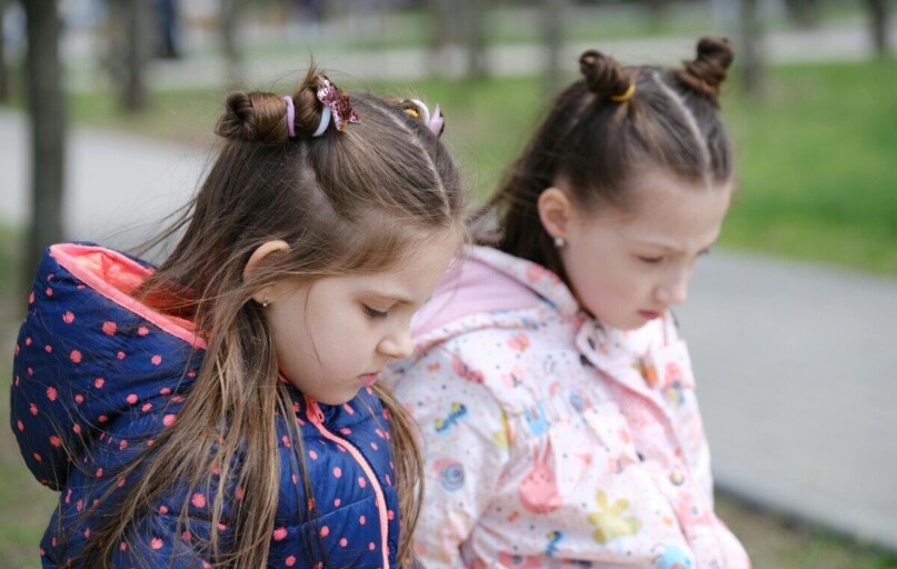 Two young girls in winter jackets, contemplative in a park setting.