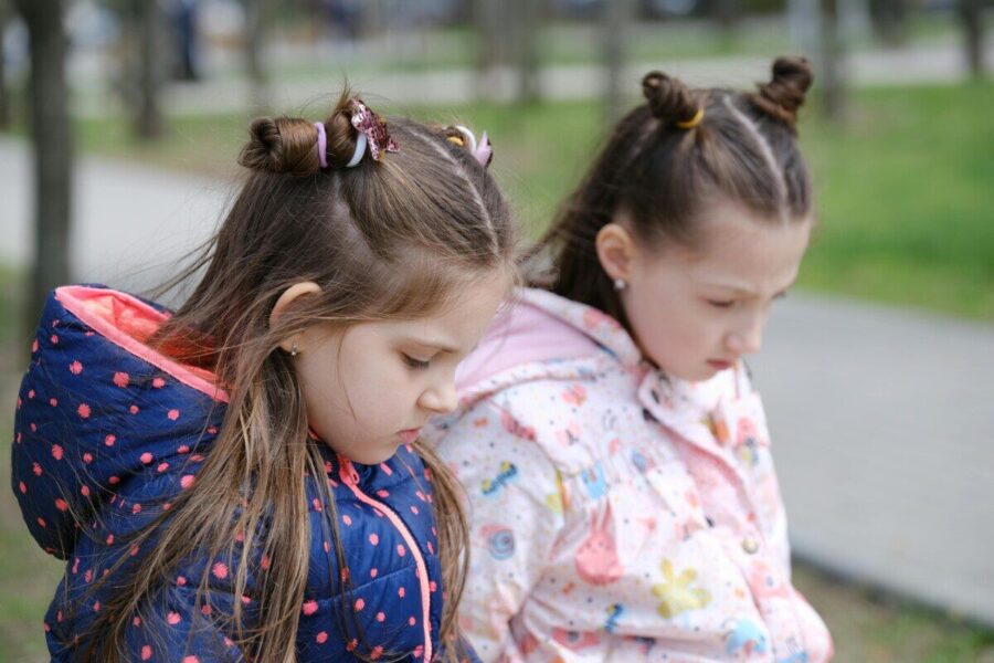 Two young girls in winter jackets, contemplative in a park setting.