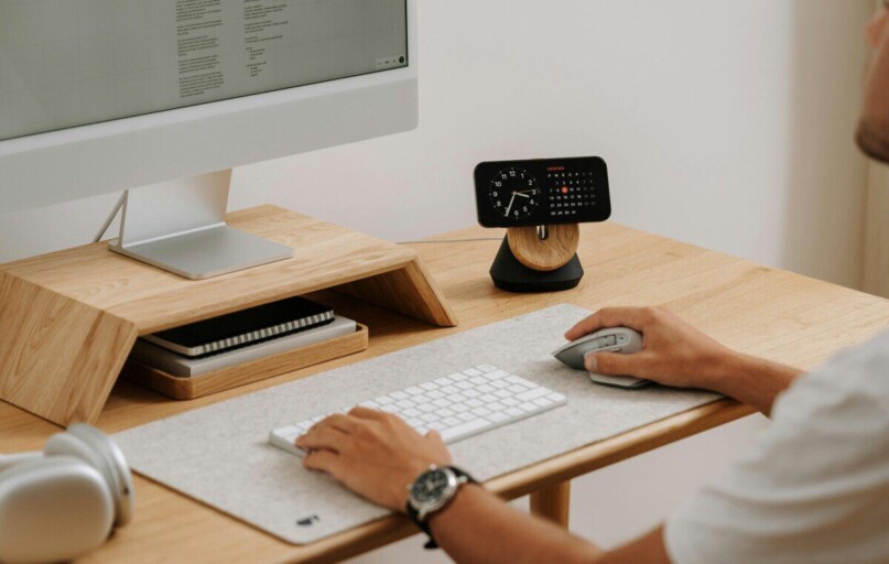 A clean and modern desk setup featuring a computer, clock, and accessories in a home office.