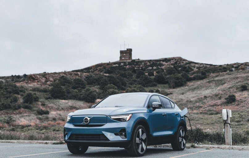 A blue Volvo electric car charging in a scenic outdoor location with a hill in the background.