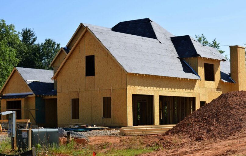 A partially built wooden house under construction, showcasing its progress and design in daylight.