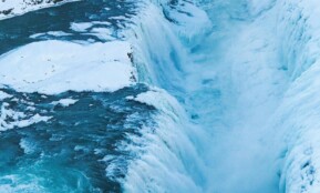 Stunning view of a frozen waterfall cascading through a snowy Icelandic gorge, capturing winter's icy beauty.