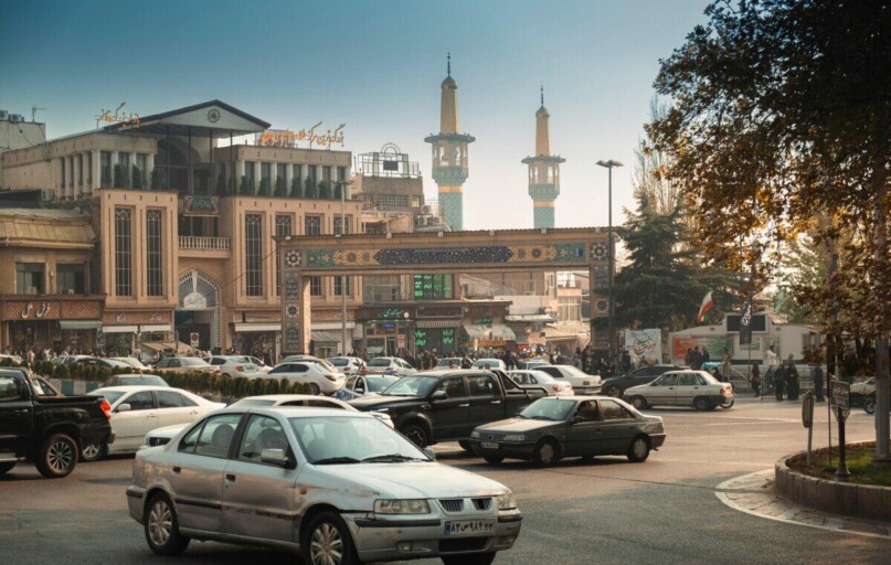 Bustling Tehran street scene with cars, mosque minarets, and traditional architecture.