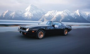 A vintage sports car speeds along a road with stunning snowy mountains in the background, exuding adventure
