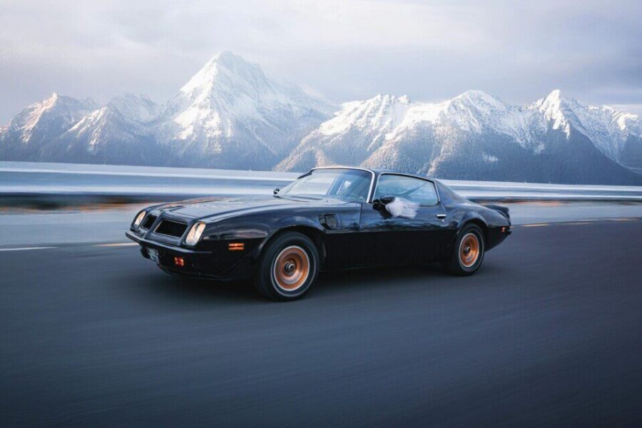 A vintage sports car speeds along a road with stunning snowy mountains in the background, exuding adventure