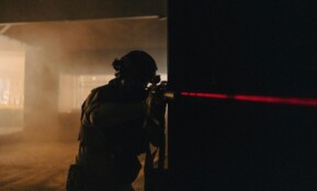 A soldier with night vision aiming with a laser sight in a dark, smoky room.