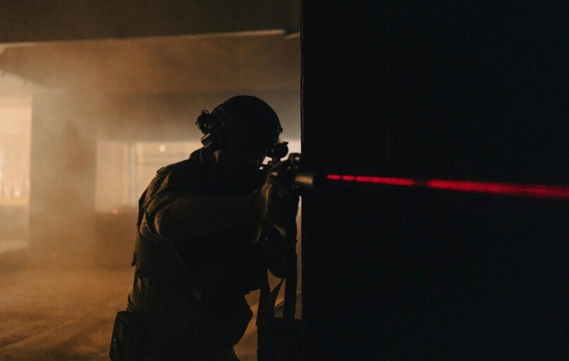 A soldier with night vision aiming with a laser sight in a dark, smoky room.