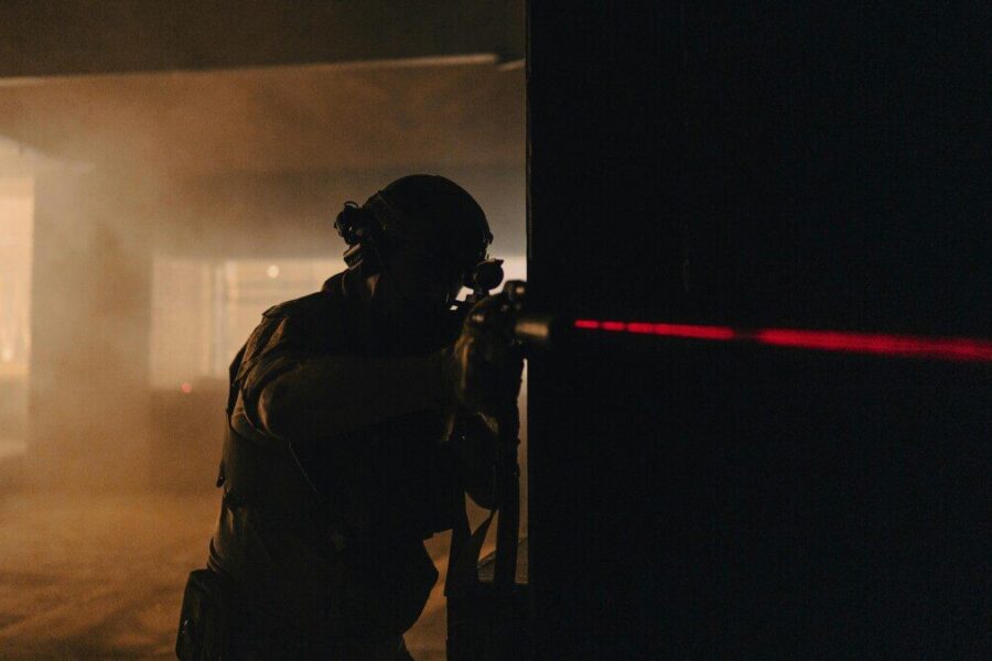 A soldier with night vision aiming with a laser sight in a dark, smoky room.