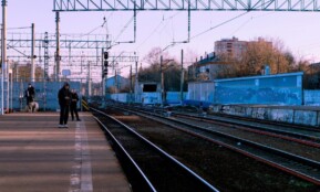A calm train station scene with people waiting on the platform during the day.
