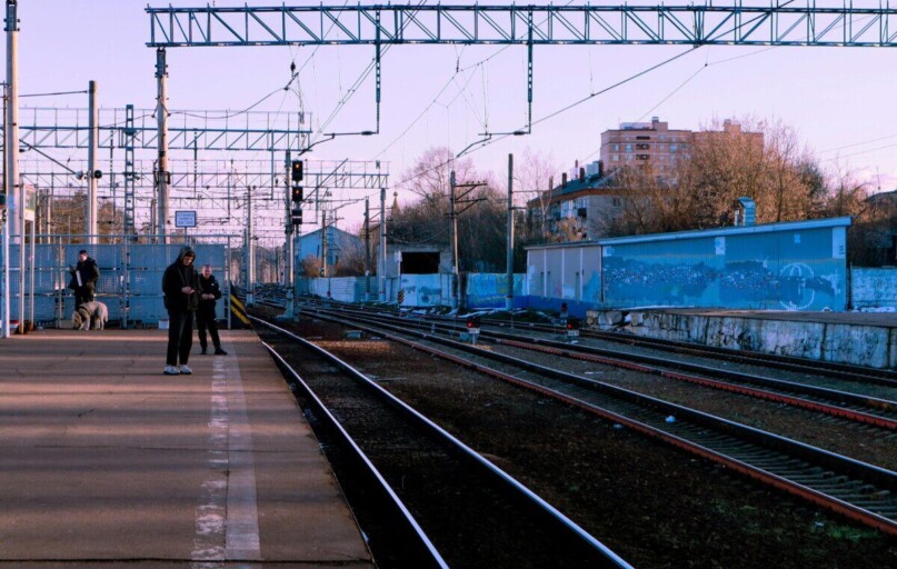A calm train station scene with people waiting on the platform during the day.