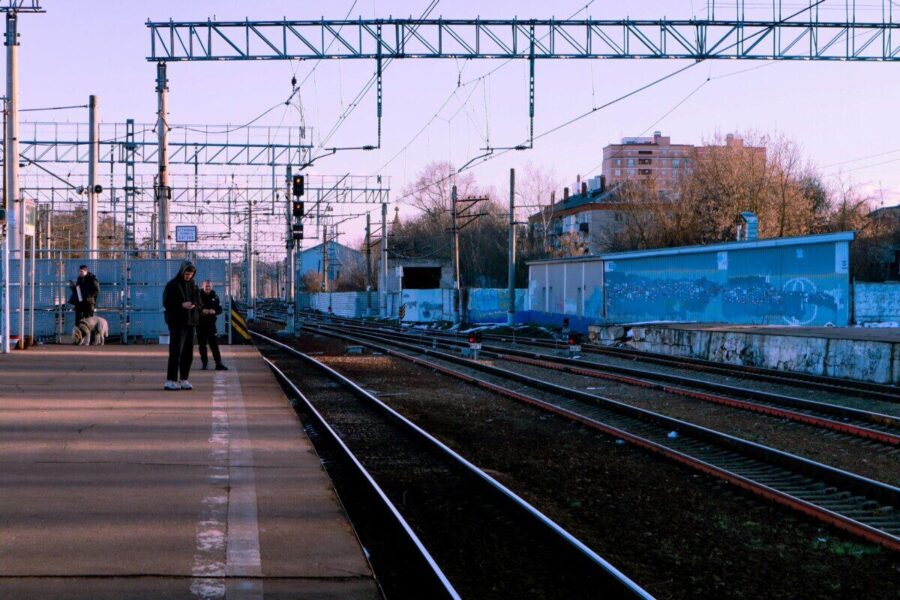 A calm train station scene with people waiting on the platform during the day.