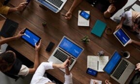 Overhead view of a diverse team discussing around a wooden table, using technology.