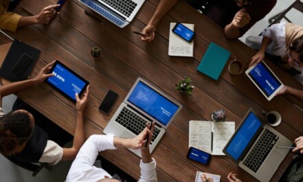 Overhead view of a diverse team discussing around a wooden table, using technology.