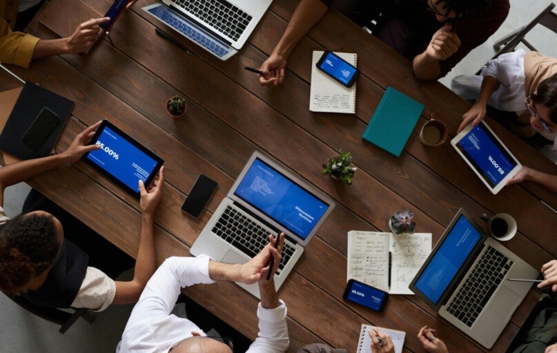 Overhead view of a diverse team discussing around a wooden table, using technology.