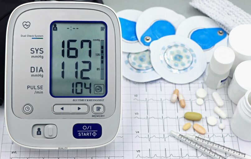 A close-up shot of medical equipment including blood pressure monitor and pills on an ECG graph.