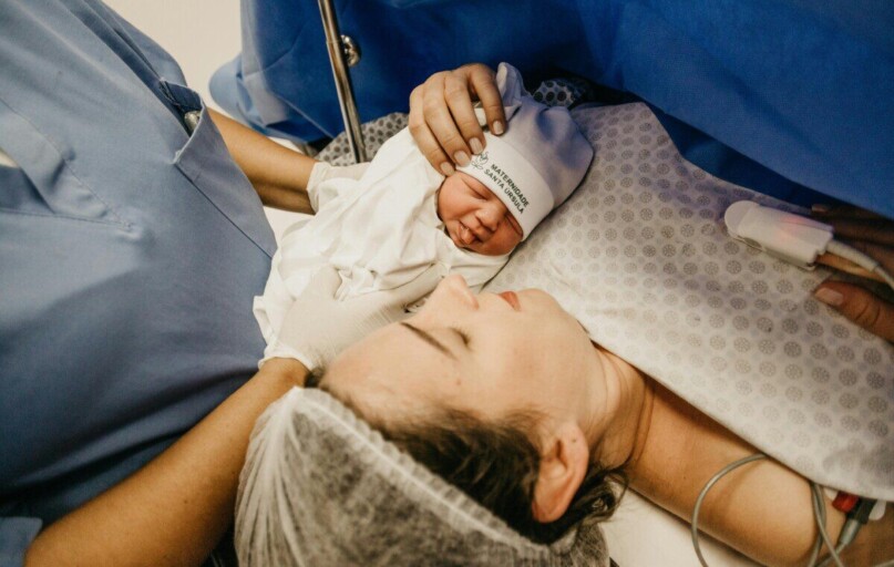A mother cradling her newborn immediately after childbirth in a hospital setting.