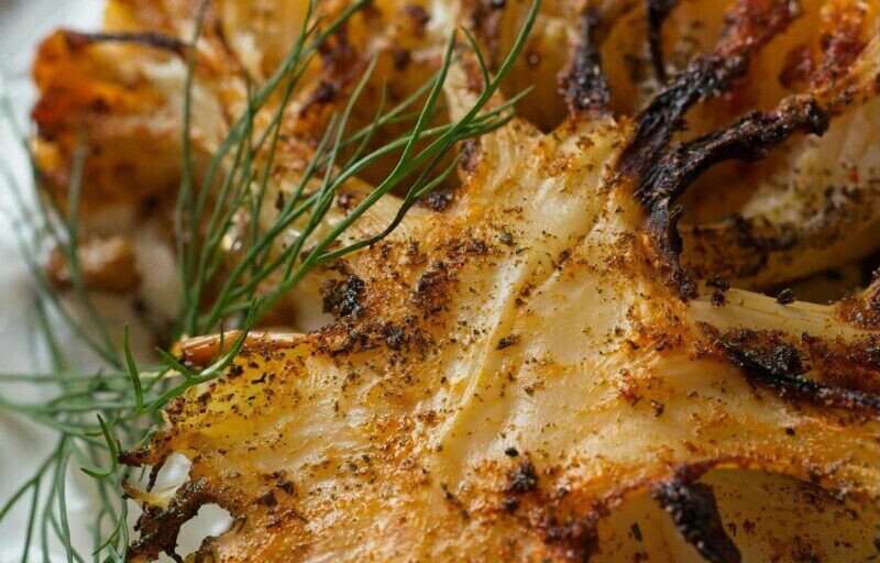 Close-up of grilled cauliflower seasoned with dill on a white plate.