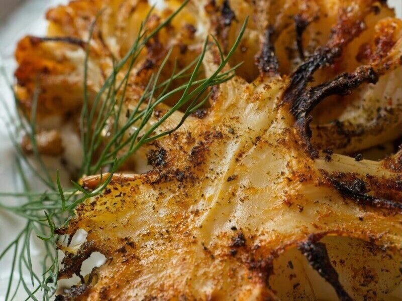 Close-up of grilled cauliflower seasoned with dill on a white plate.