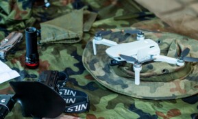 Compact white drone on camouflage gear, surrounded by flashlight and tools.