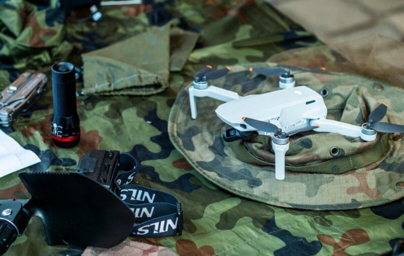 Compact white drone on camouflage gear, surrounded by flashlight and tools.