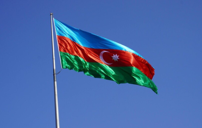 The national flag of Azerbaijan waves against a clear blue sky, symbolizing national pride.