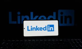 Smartphone showing LinkedIn logo with keyboard and large background logo, business theme.