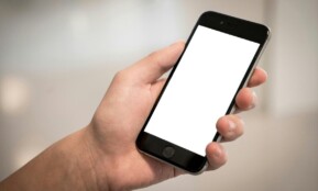 A hand holding a modern smartphone with a blank screen, ideal for design mockups.