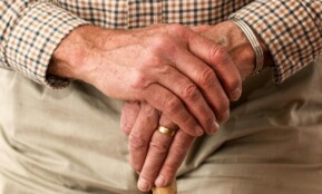 A detailed image of elderly hands clasping a wooden cane, symbolizing aging and support.