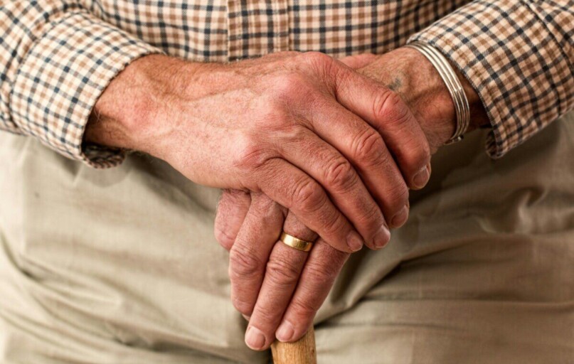 A detailed image of elderly hands clasping a wooden cane, symbolizing aging and support.