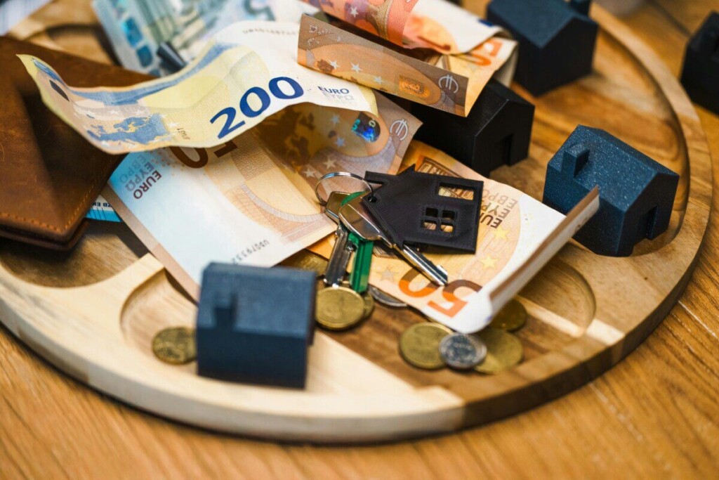 Euro currency, keys, and miniature houses symbolize real estate and finance concepts.