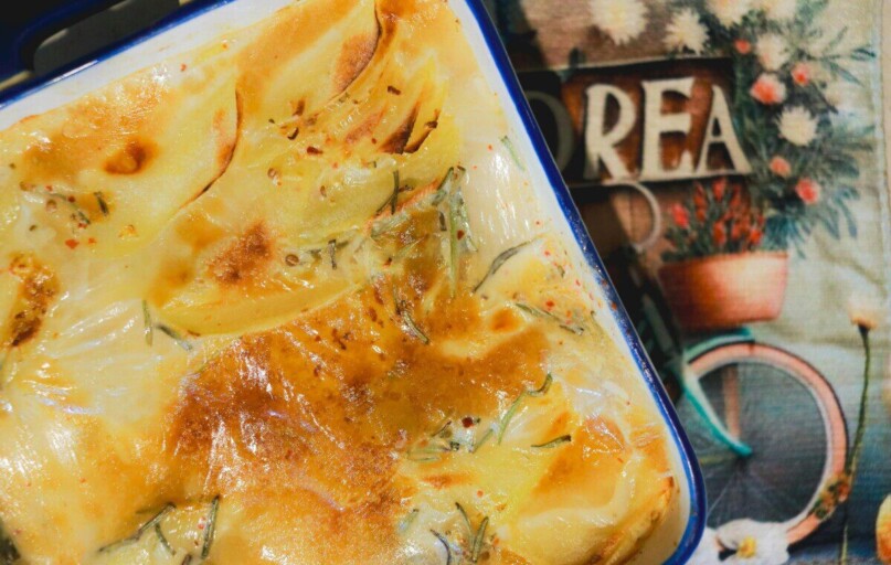 A rich and creamy potato gratin freshly baked, golden and crispy in a ceramic dish.