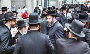 Group of Orthodox Jewish men gathered on a busy street in New York City.