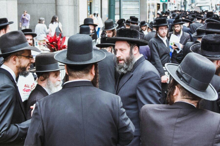 Group of Orthodox Jewish men gathered on a busy street in New York City.