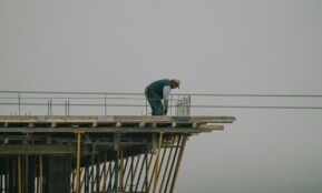A construction worker bends over rebar on a high framework under a foggy sky in Denizli, Türkiye.