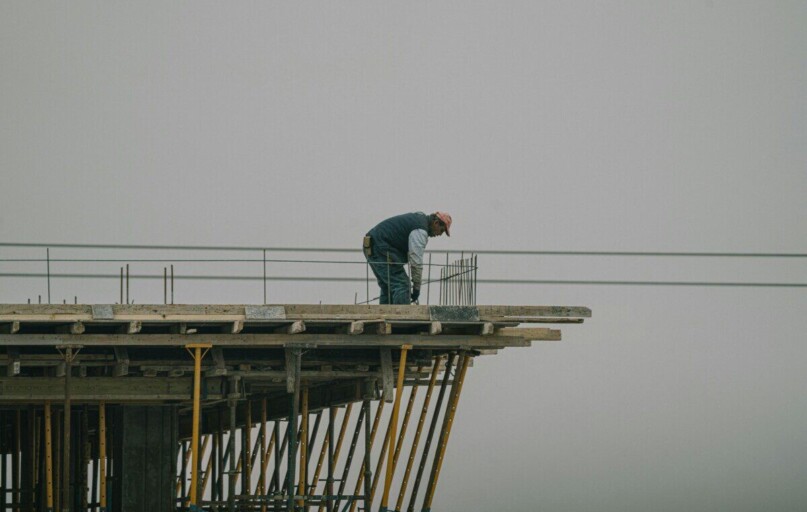 A construction worker bends over rebar on a high framework under a foggy sky in Denizli, Türkiye.