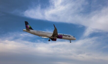 A commercial airplane flying against a vibrant blue sky with clouds.