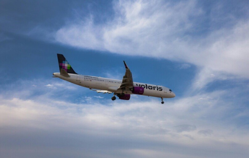 A commercial airplane flying against a vibrant blue sky with clouds.