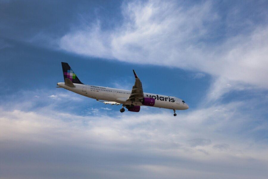 A commercial airplane flying against a vibrant blue sky with clouds.