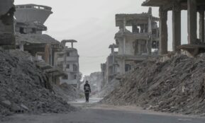 A solitary figure walks through the devastated ruins of Damascus, Syria, highlighting the aftermath of conflict.