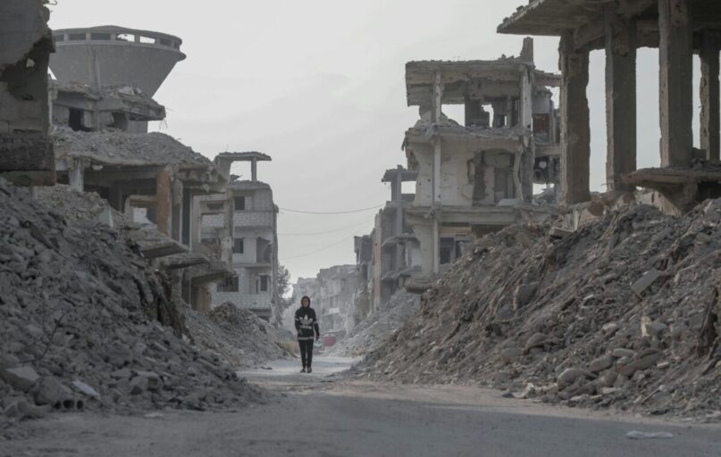 A solitary figure walks through the devastated ruins of Damascus, Syria, highlighting the aftermath of conflict.