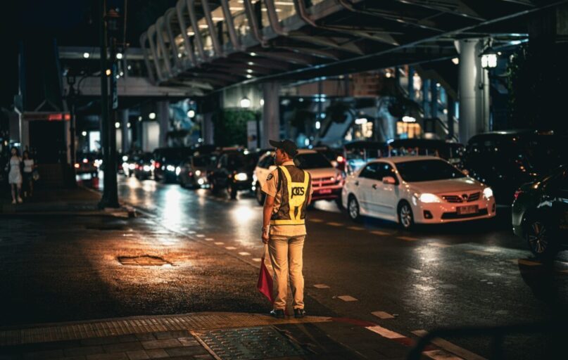 Traffic officer directs busy street traffic at night in Bangkok, Thailand.