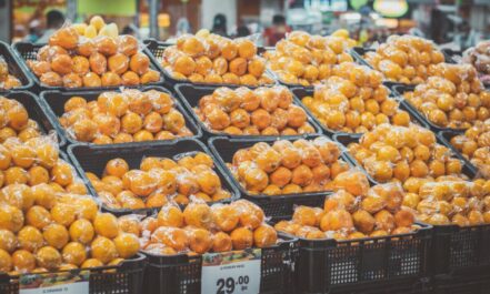 Stack of fresh oranges wrapped in plastic at a grocery store, priced with tags.