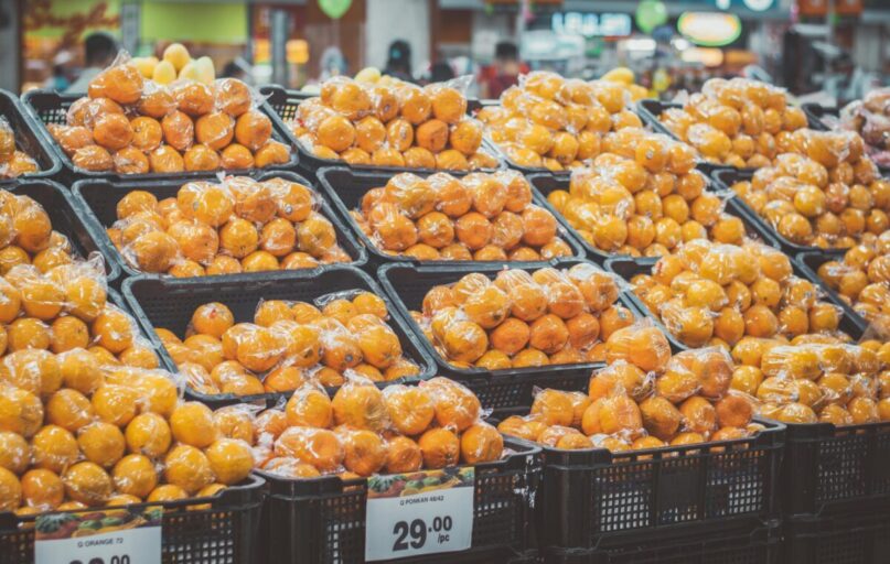 Stack of fresh oranges wrapped in plastic at a grocery store, priced with tags.